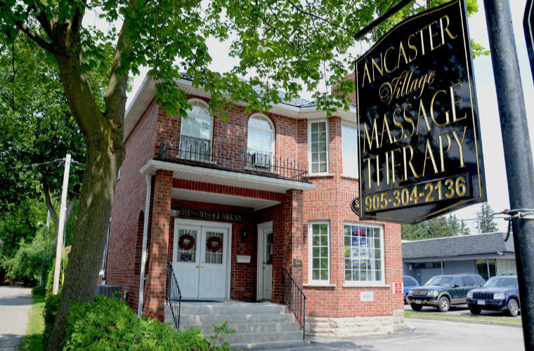 A red brick house with a sign for Ancaster Village Massage Therapy in the foreground.