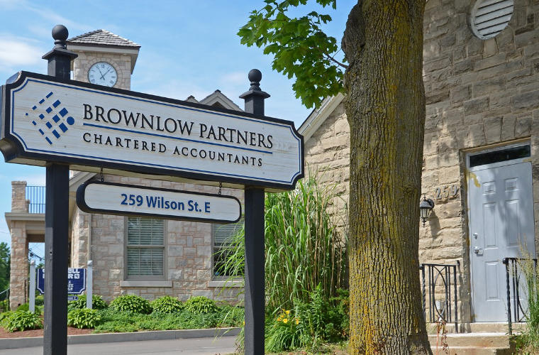 A rough hewn beighe stone building with a sign for Brwnlow Partners Chartered Accountants on the front lawn.