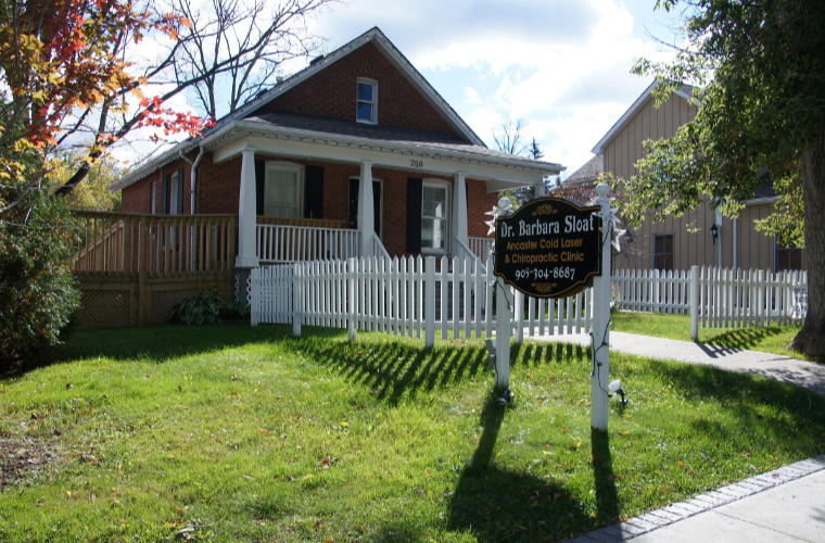 A red brick house with a white picket fence and a sign for Dr. B. Sloat on the front lawn.