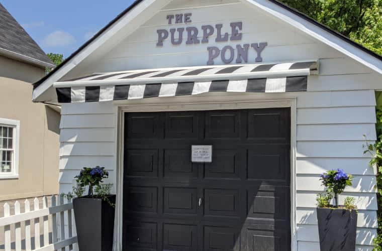 A white garage with black door and a sign for The Purple Pony above it.
